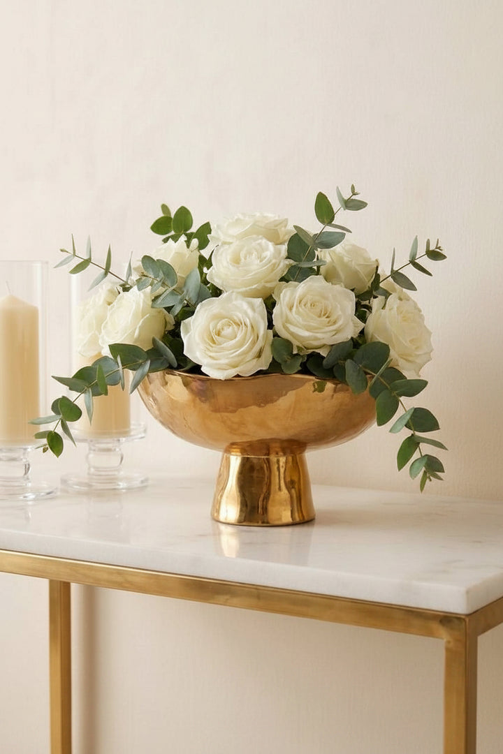 Decorative setup with a gold bowl containing white flowers on a marble surface.